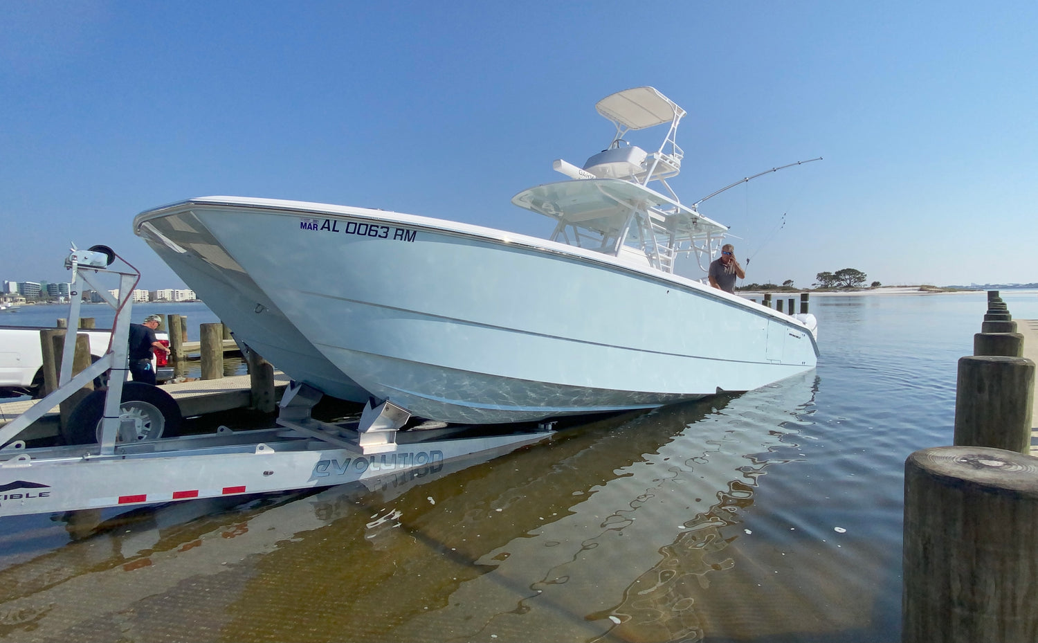 Light blue and white sport fisher being trailered out of the water. Blue skies and city line in background.